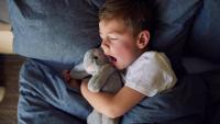 kid yawning in bed with stuffed bunny